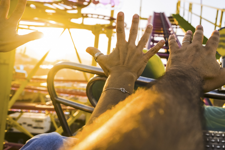 Pov of Couple on a roller coaster with arms in the air amused and excited waiting for the steep descent. Sunny afternoon with fun. Concept of free time and cheerfulness
