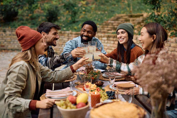 Happy friends toasting while eating at picnic table on a patio.