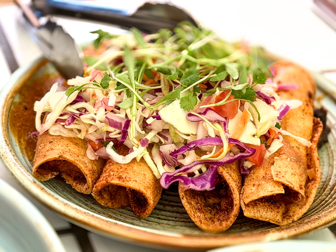 Crispy rolled tacos topped with fresh slaw and herbs on a plate